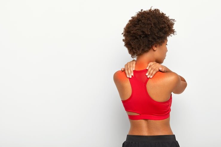 back view young curly woman suffers from neck pain osteoporosis has painful feelings muscles holds hands near shoulders wears red top 273609 33730